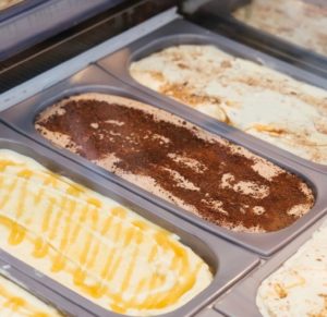 Close up of three different ice cream tubs in a glass window cabinet