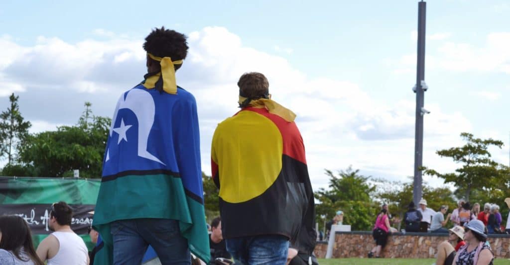 Two people wearing the Aboriginal Flag and Torres Strait Island Flag over their backs