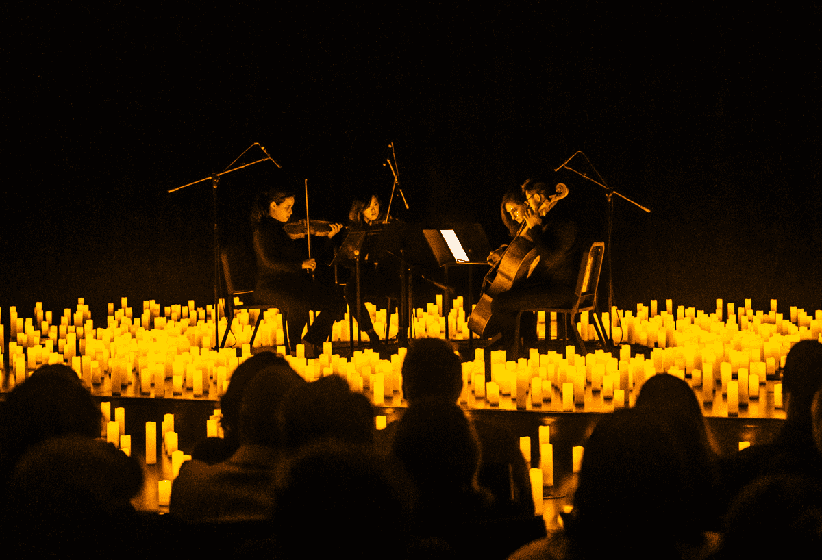 The silhouette of an audience watching a string quartet perform on a stage covered in candles.