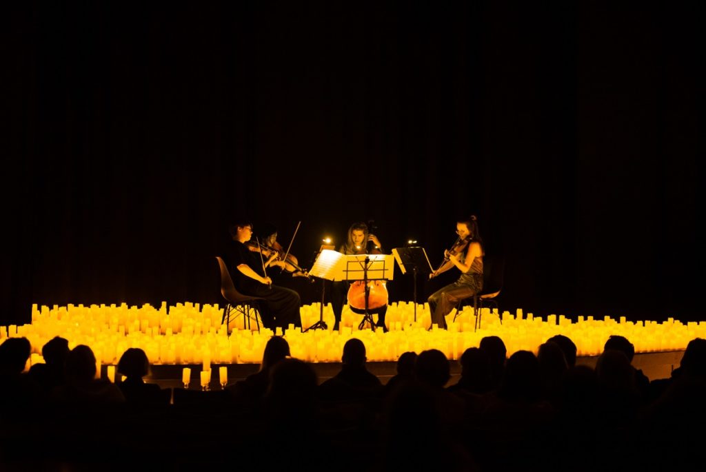 Three musicians play their instruments surrounded by hundreds of flameless candles.