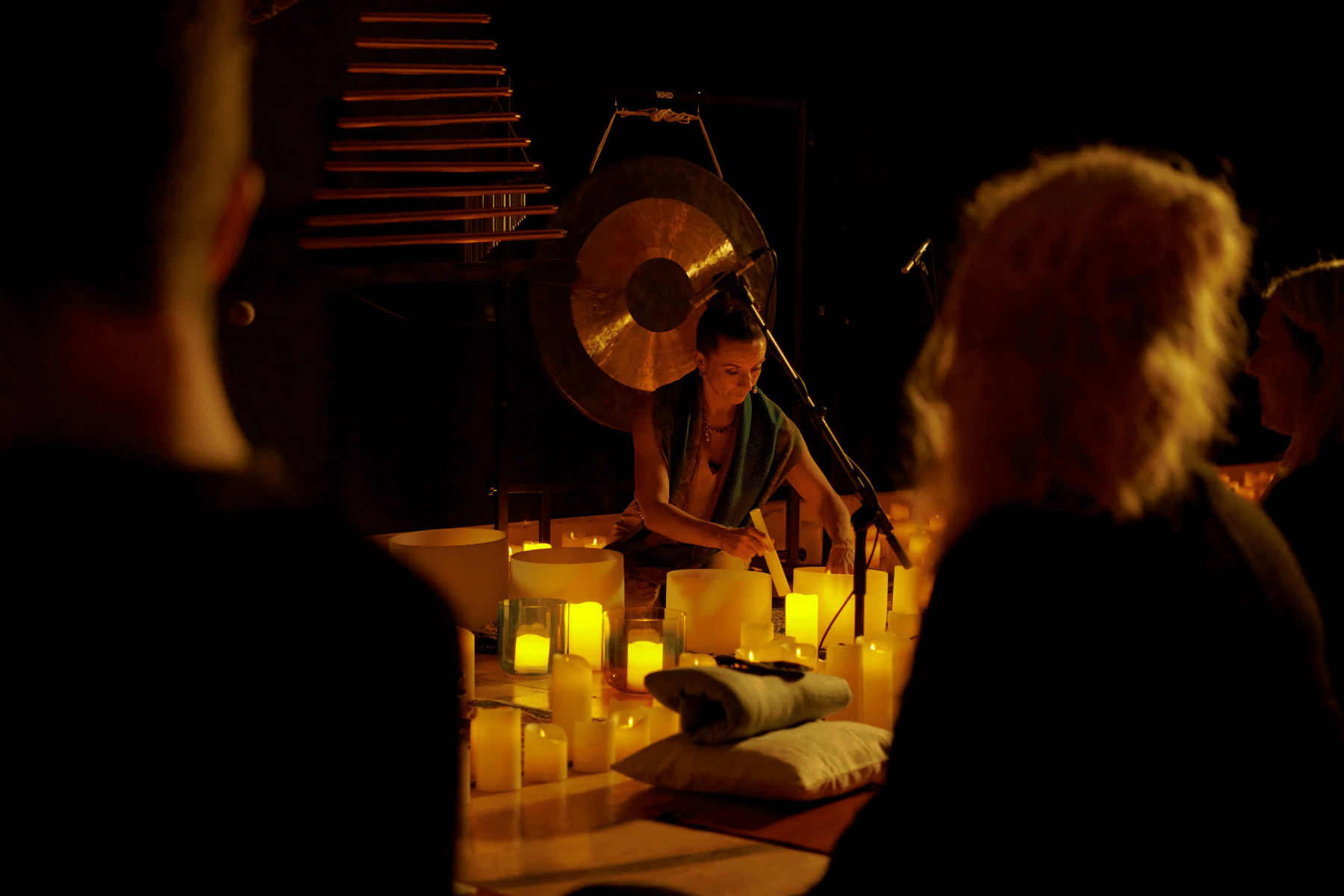 An instructor at a Mindful Glow experience carrying out sound therapy with the silhouette of two guests watching her.