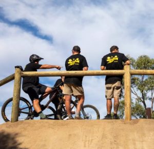 Three people standing on a dirt viewing deck of the mountain bike trail