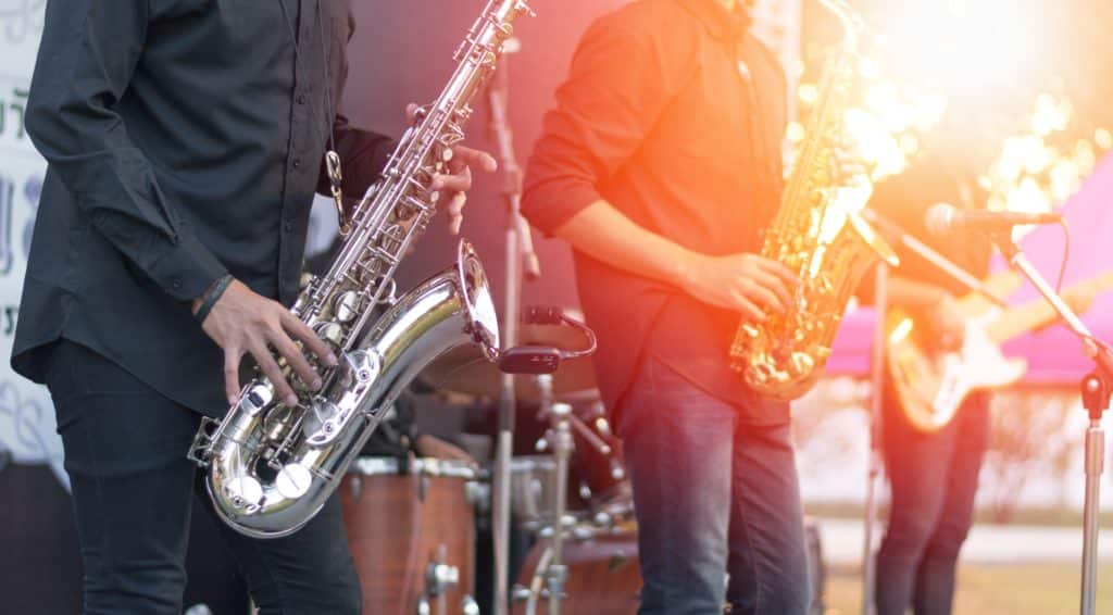 Three people playing saxophone in daylight on stage