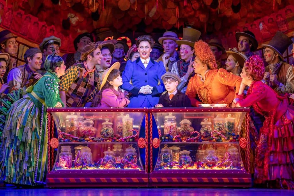 Mary Poppins cast on stage performing behind a cabinet filled with lollies