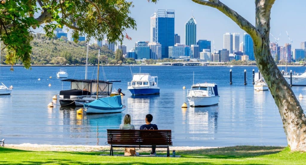 Two people sitting on a bench overlooking the Swan River and Perth city and background