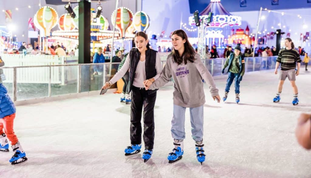 Two people holding hands while skating on an indoor ice rink