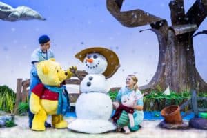 Winnie the pooh life-size puppet on stage with puppeteer, next to snowman puppet and piglet puppet in a winter scene
