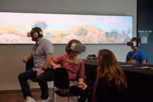 Three people sitting with VR goggles over their eyes and head