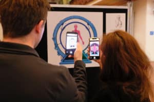 Two people holding up phones and scanning an image on the wall